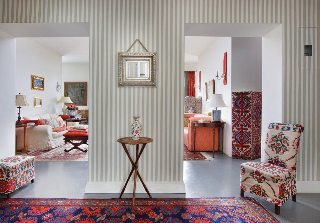 Continuous, open-plan interior belonging to collector: mixture of patterns and styles with Oriental rugs, colourful textiles and grey and white striped wallpaper