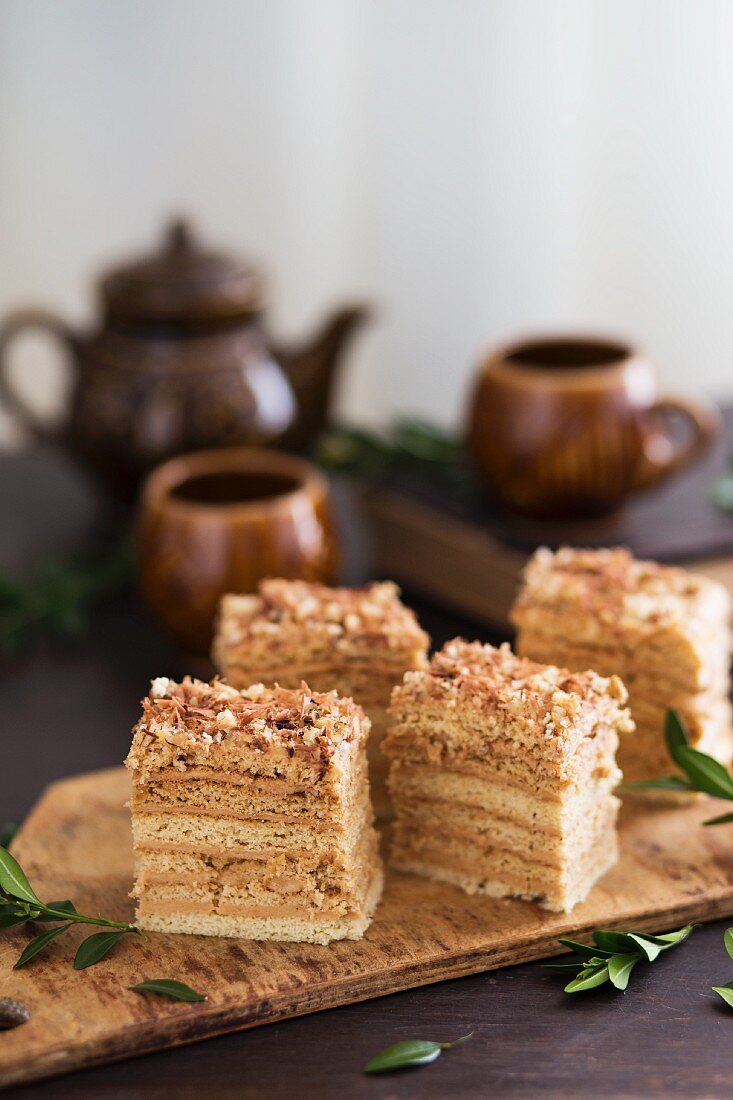 Geschichteter Honigkuchen mit Walnüssen auf rustikalen Holzbrett vor Teetassen und Teekanne