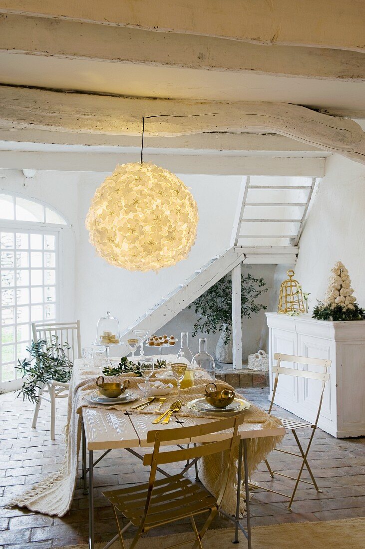 Rustikale, weiss getünchte Holzdecke mit großer Blumen-Ballonlampe und darunter stehendem, gedeckten Weihnachtstisch