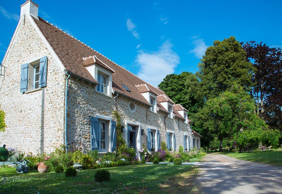 Renoviertes Natursteinhaus mit Staudenbeeten in offenem Vorgarten und Auffahrt