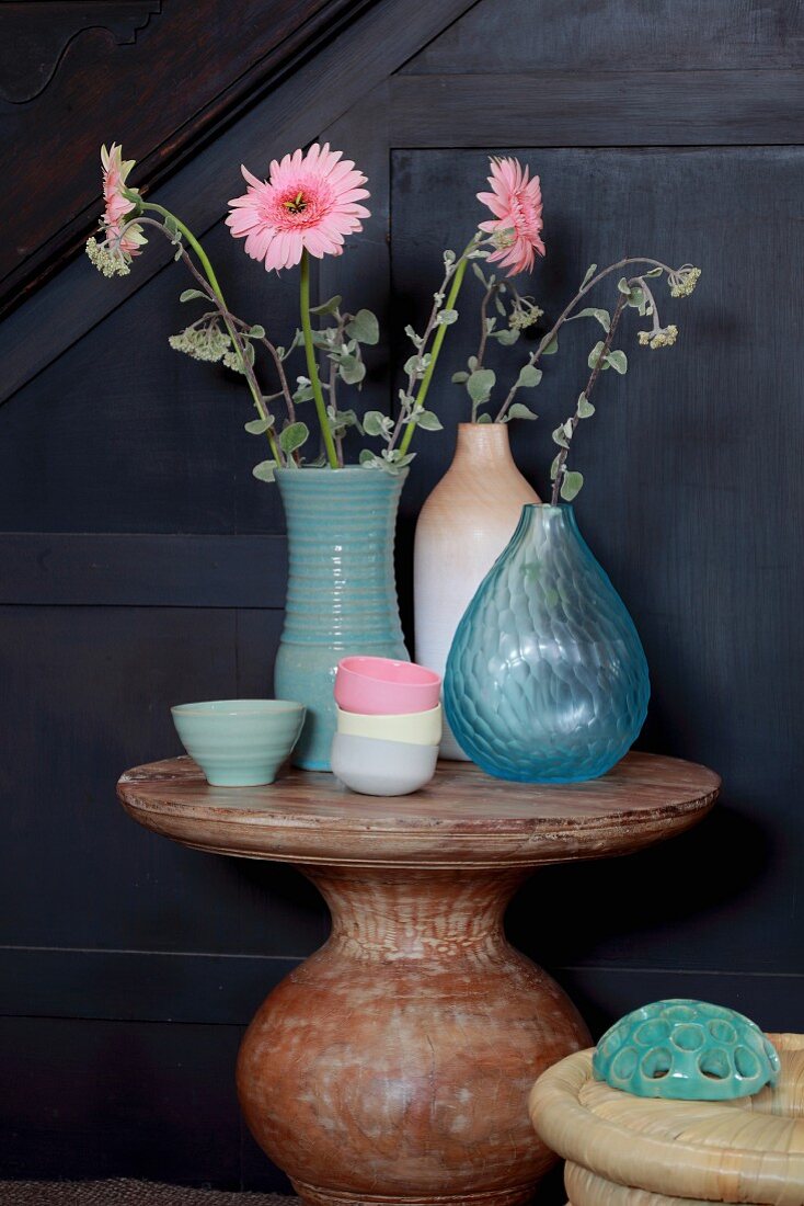 Pink gerbera daisies in various vases and pastel bowls on round stone table
