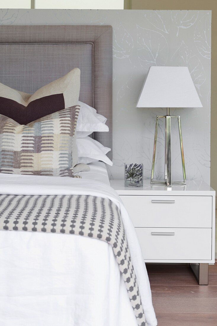 Patterned blanket on bed and table lamp on white bedside cabinet