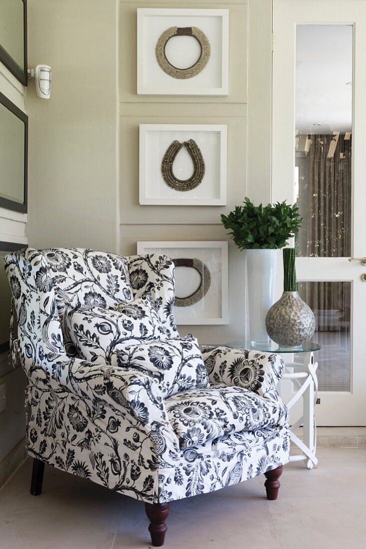 Black and white floral armchair in front of framed necklaces