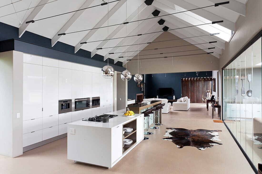 Moderne Satteldachkonstruktion mit Zugstäben über einem langgestreckten Wohnraum mit zentraler Designerküche