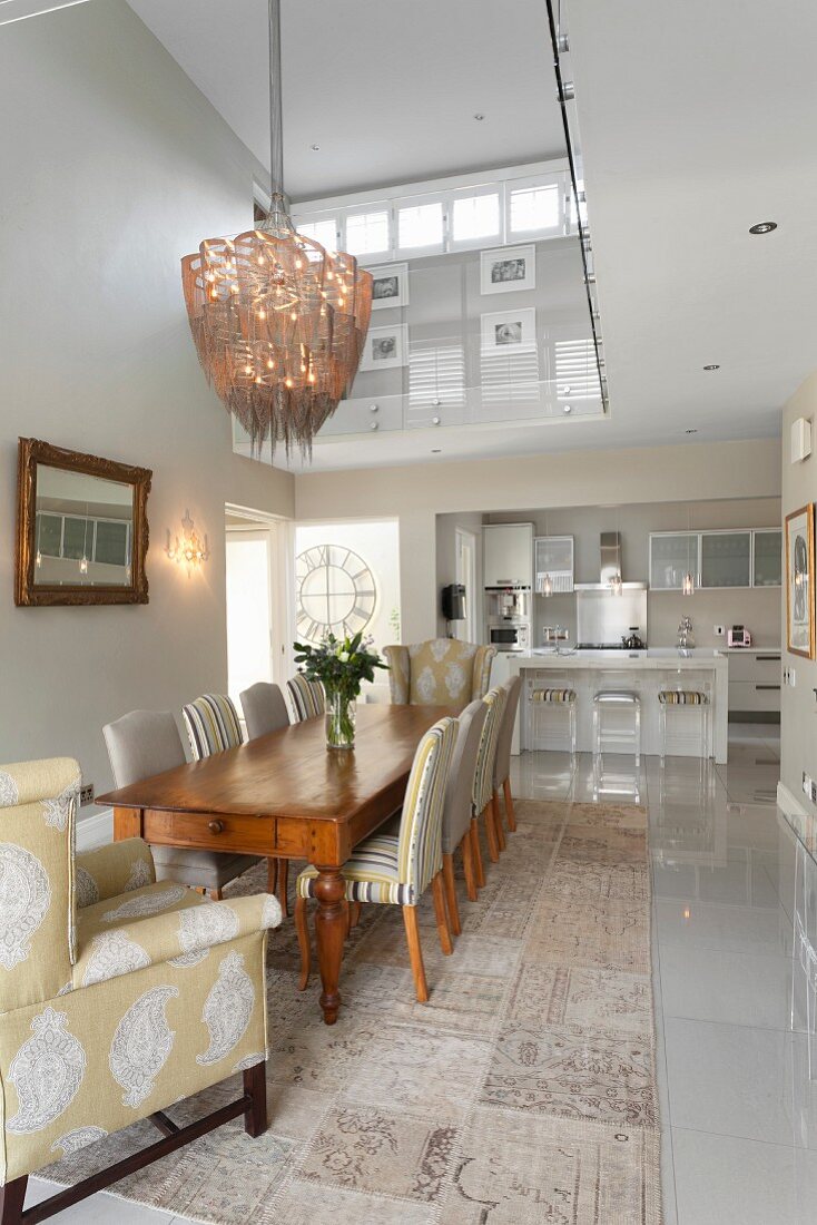 Classic dining room in shades of green and grey with elegant upholstered chairs and view into open-plan kitchen