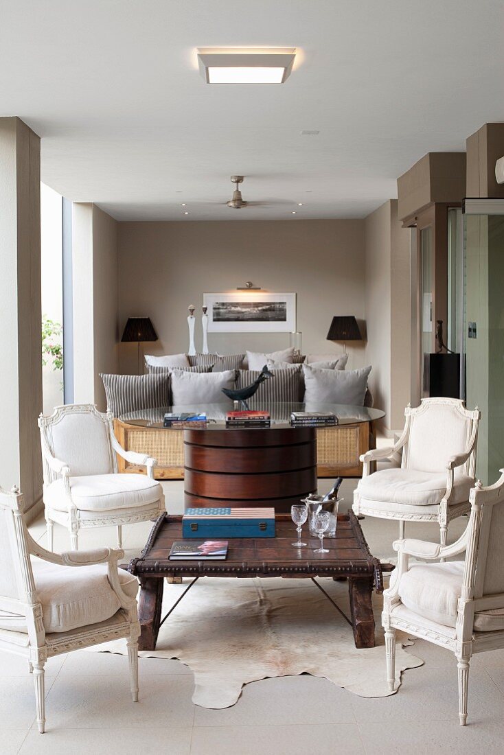 Four white Baroque-style chairs around Colonial-style coffee table in front of Art Deco table