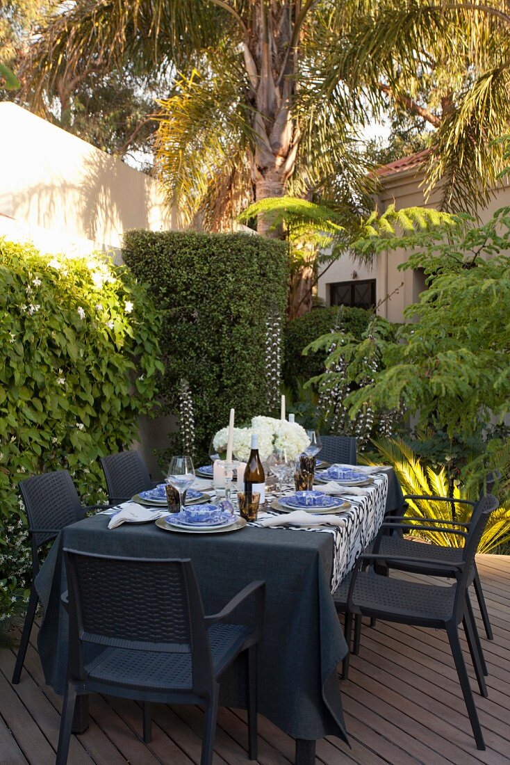 Terrasse im Innenhof mit gedecktem Tisch, schwarzen Gartenmöbeln und bewachsener Mauer