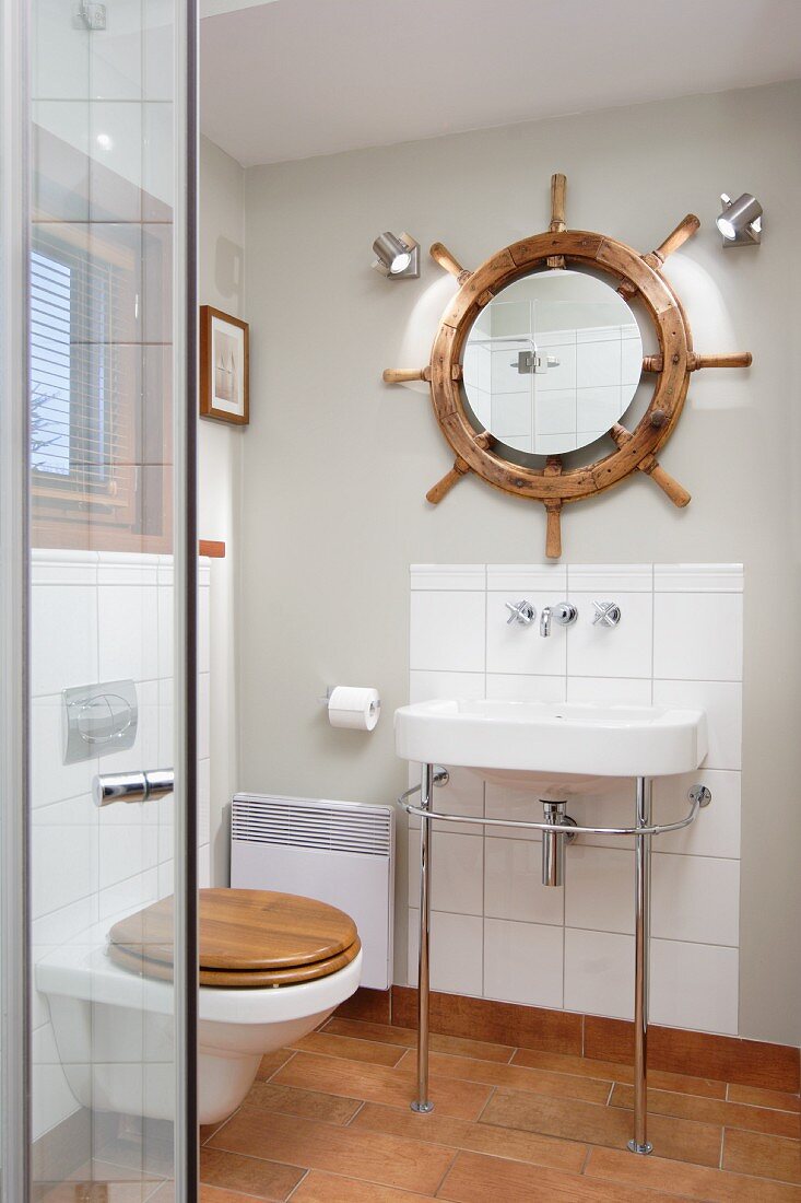 Washstand with metal frame against small tiled splashback below mirror in centre of ship’s wheel on wall of modern bathroom