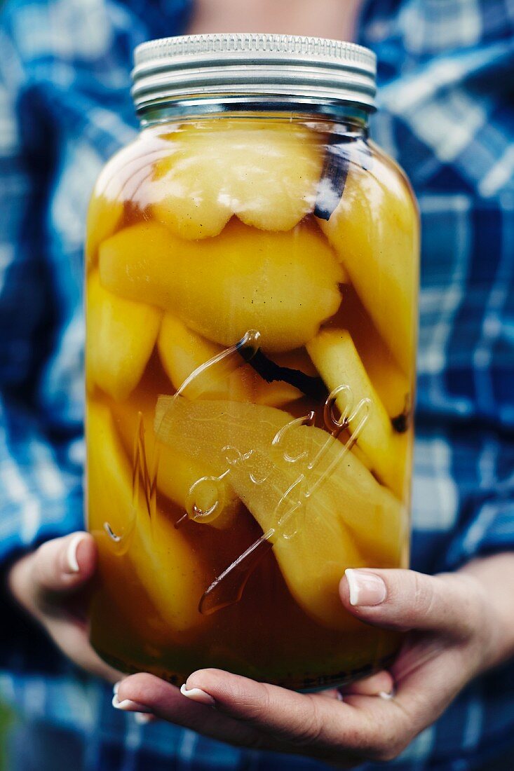 A woman holding a jar of preserved caramel pears