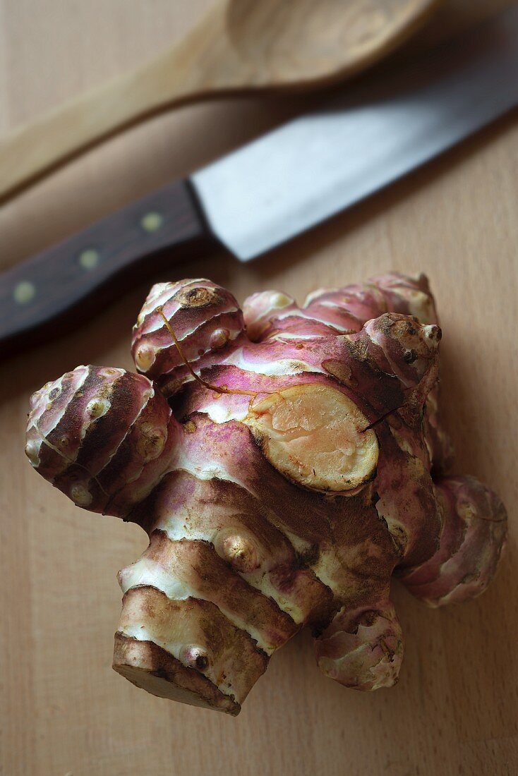 A Jerusalem artichoke on a chopping board with a knife and a wooden spoon