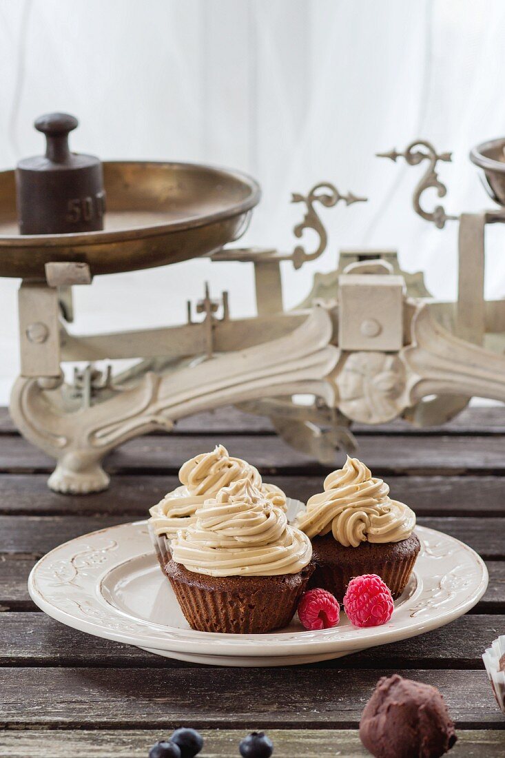 Schokoladencupcakes mit Buttercreme und frischen Beeren auf altem Holztisch vor Fenster