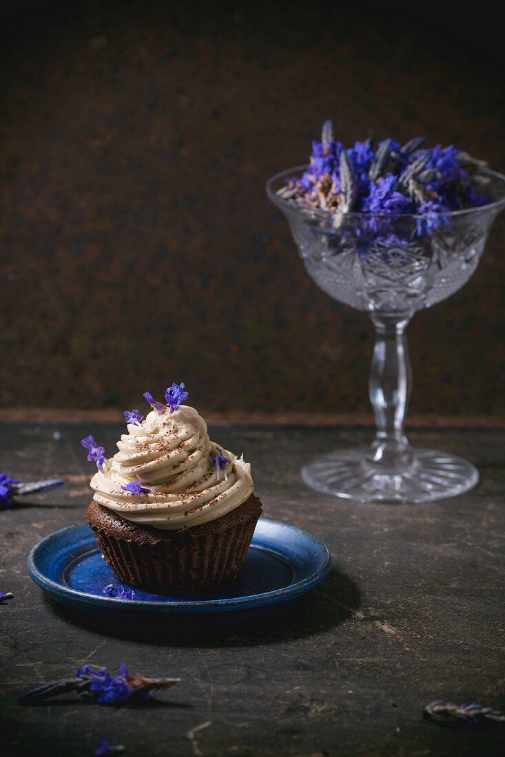 A chocolate cupcake with coffee buttercream and lavender flowers on a blue plate