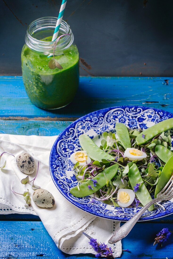 A mixed leaf salad with young peas and quail's eggs served with a herb smoothie on a blue wooden table