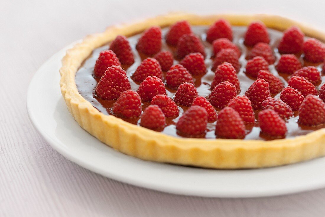A tart with a shortcrust pastry base, topped with chocolate cream and fresh raspberries