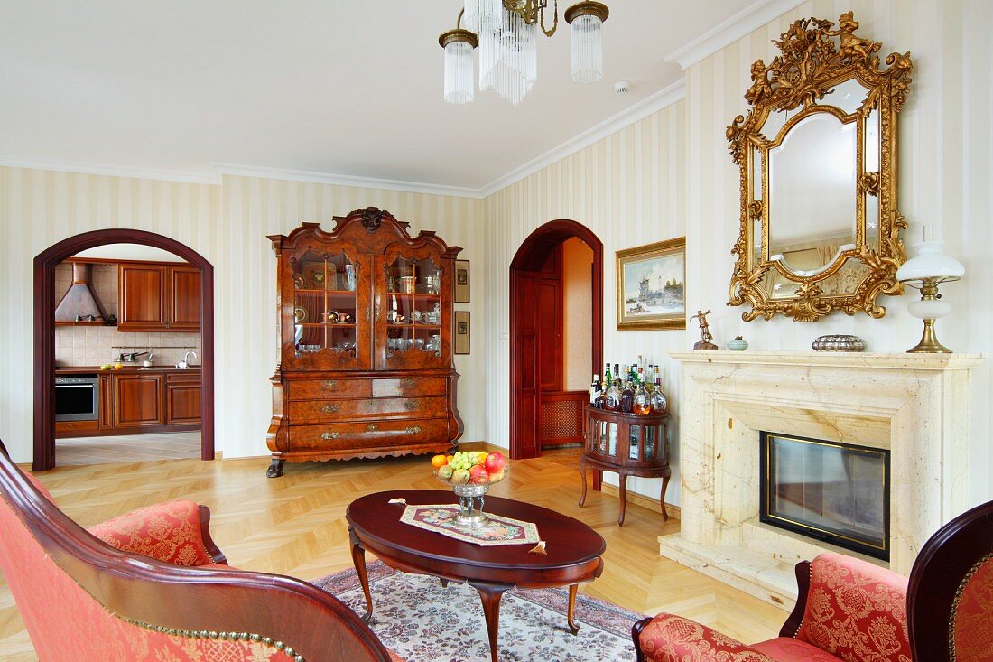 Lounge area with antique coffee table in front of fireplace and mirror with carved, gilt frame on wall in grand living room