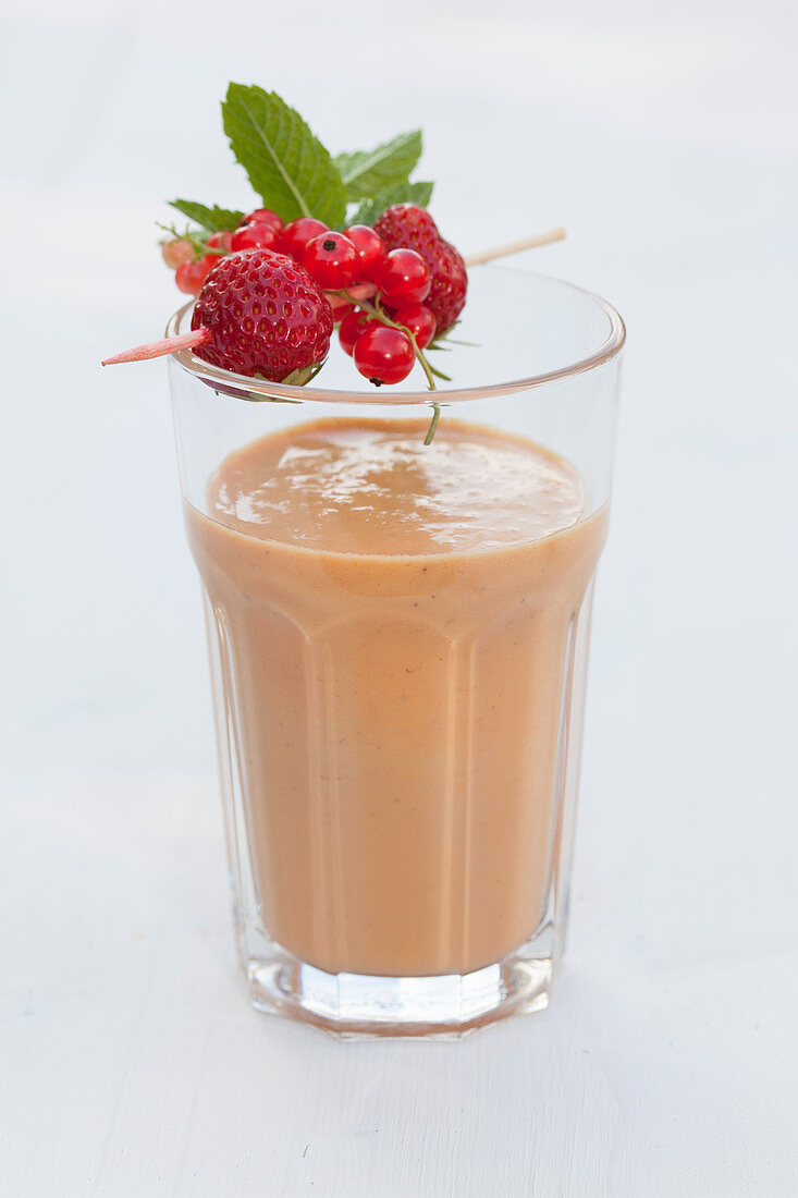 A glass of coconut and macadamia nut smoothie with strawberries garnished with a fruit and mint skewer