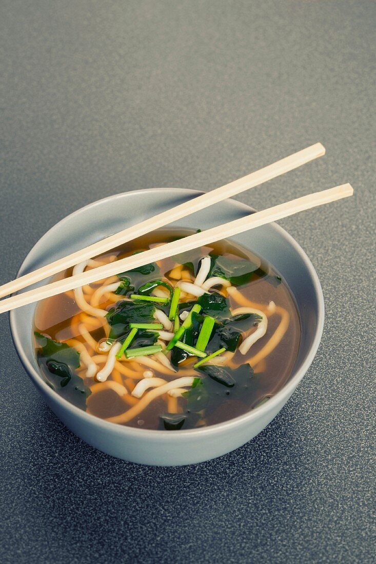 A bowl of Japanese udon noodle soup, algae, chives and chopsticks