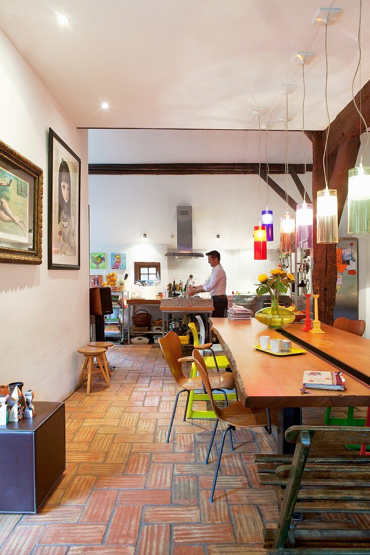 Live-edge wooden dining table and retro chairs on terracotta-tiled floor with kitchen in background