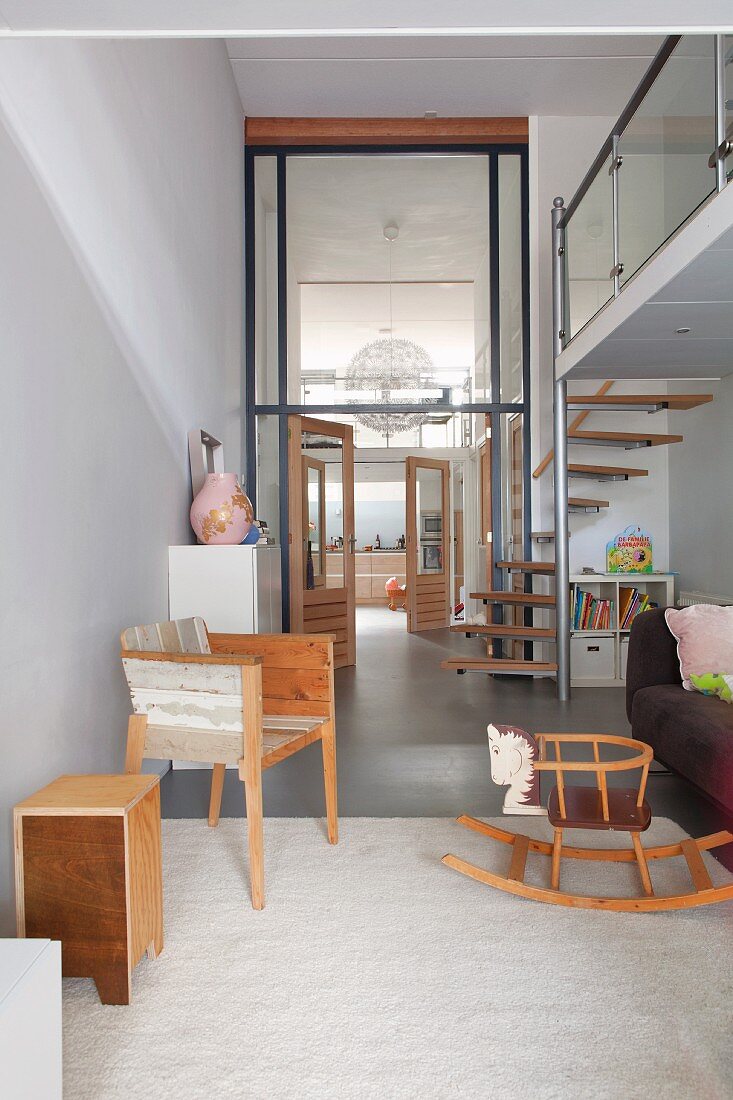 Open-plan, modern living area with spiral staircase leading gallery, retro rocking horse and view through interior window into high-ceilinged foyer and kitchen