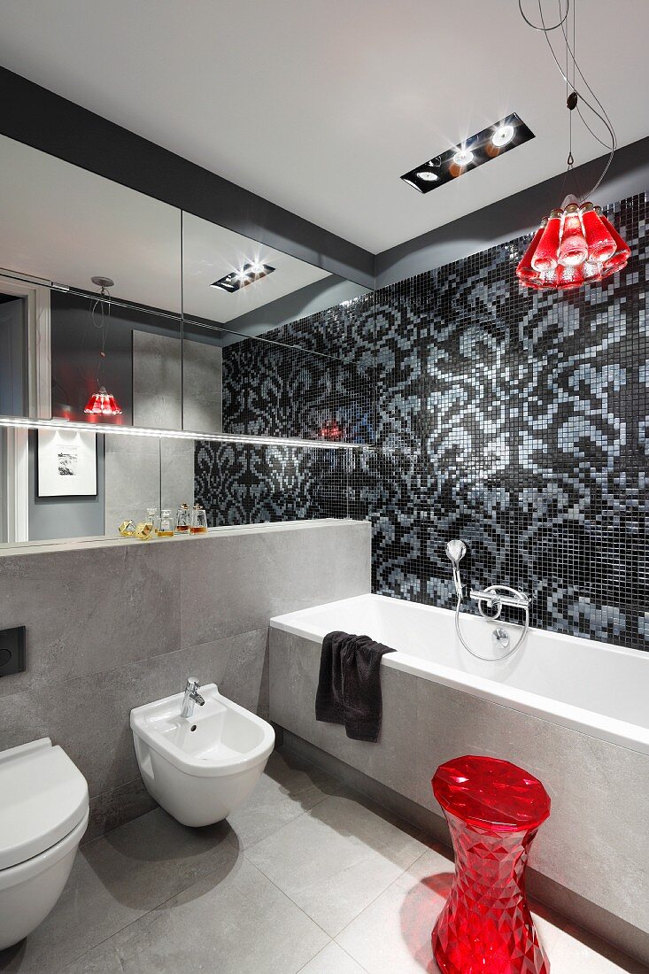 Designerbad in Grautönen mit roten Farbakzenten, 'Campari Light' Pendelleuchte vor schwarz-grau gefliester Wand mit floralem Muster