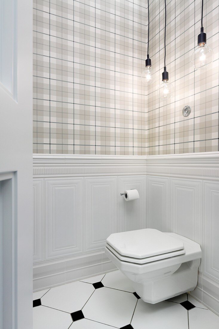 Toilet mounted on wainscoting below Bulb lamps against tartan wallpaper