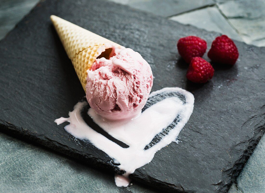 Raspberry ice cream in a cone in a heart-shaped pool of ice cream