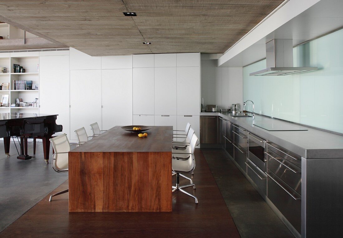 Minimalist, solid-wood dining table and classic swivel chairs in open-plan kitchen with concrete ceiling