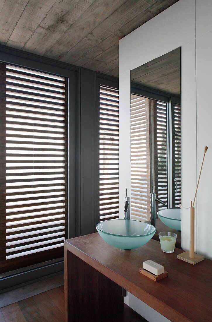 Washing area with glass basin on minimalist wooden washstand and French windows with closed wooden louvres