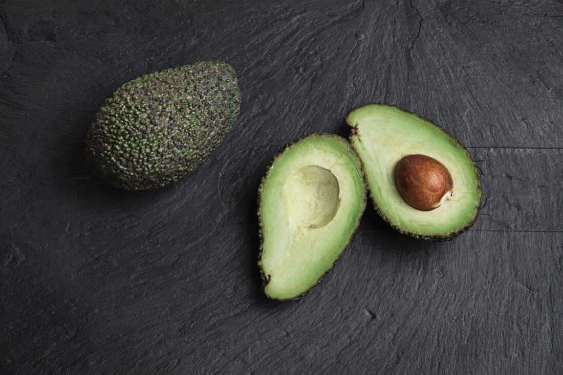 Avocados, whole and halved, on a slate platter