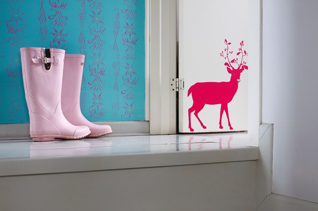 Pink child's wellingtons on platform next to white-painted wooden door with red stag motif
