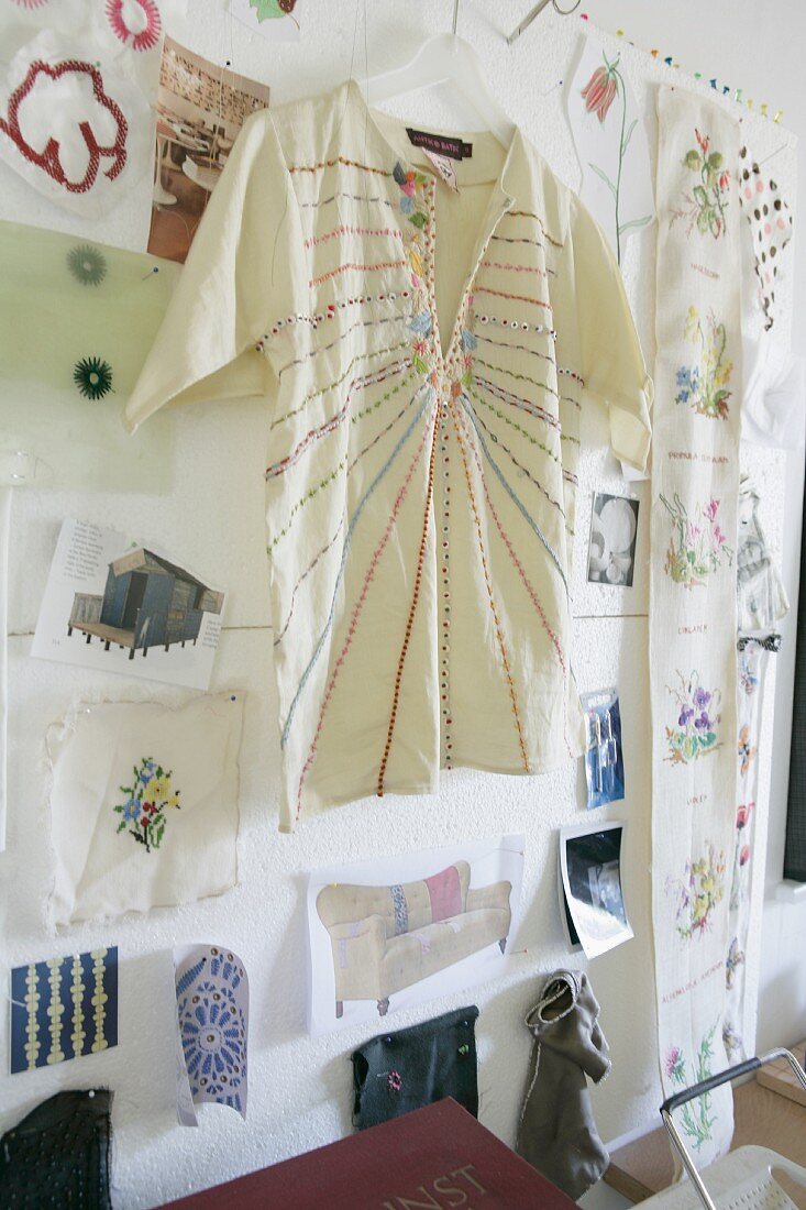 Besticktes Hemd auf Kleiderbügel vor Bildern an Wand, gehängt