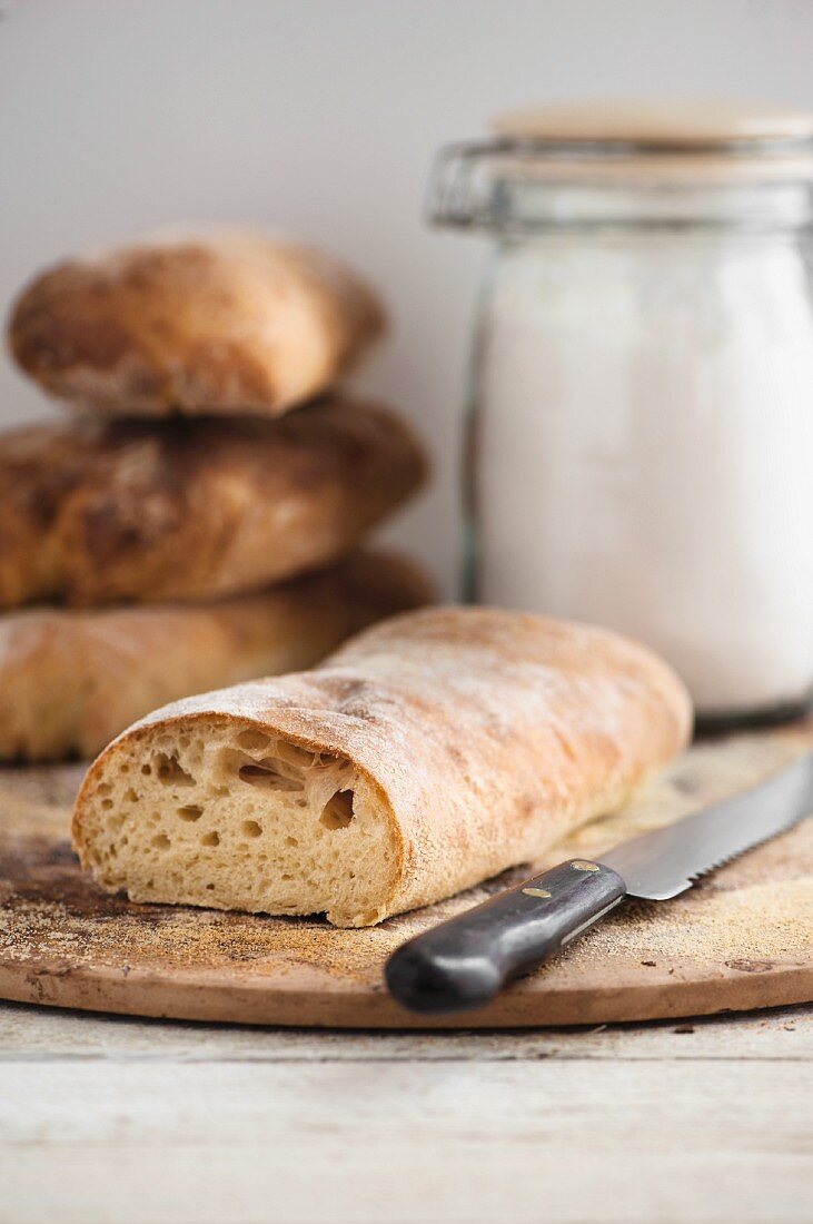 Ciabatta-Brot, angeschnitten, Brotmesser und Vorratsglas mit Mehl