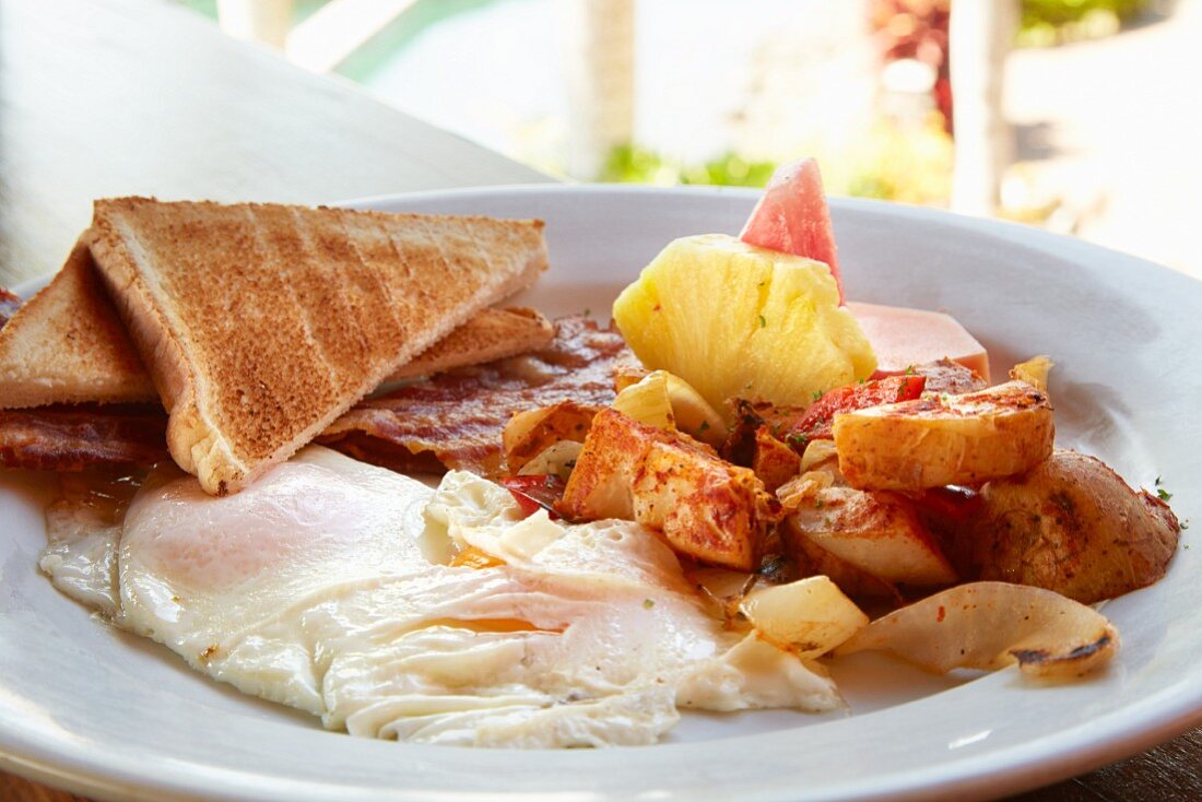 Breakfast of fried eggs, bacon, potatoes, toast and pineapple (Costa Rica)