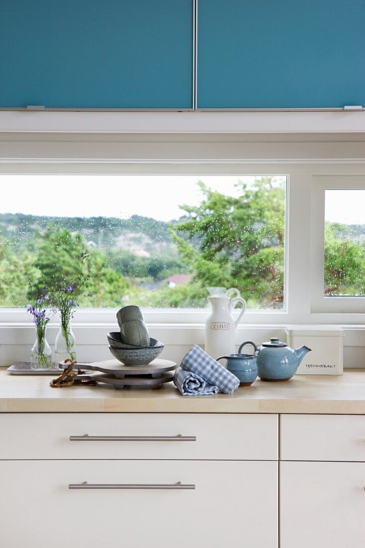 Detail of kitchen counter; wooden worksurface on white base units below window and blue wall-mounted units