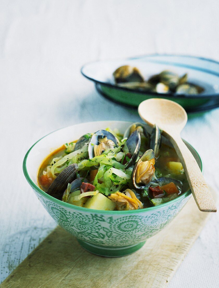 Pointed cabbage stew with mussels in a patterned bowl with a wooden spoon