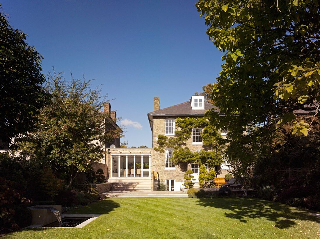 View from garden with tall trees to traditional English house with extension