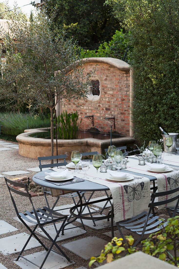 Set table in front of stone pool with water spout in garden