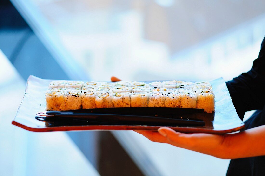 A woman holding a tray of maki sushi