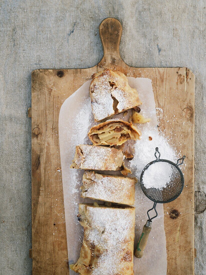 Apple strudel with an icing sugar sieve on a wooden board