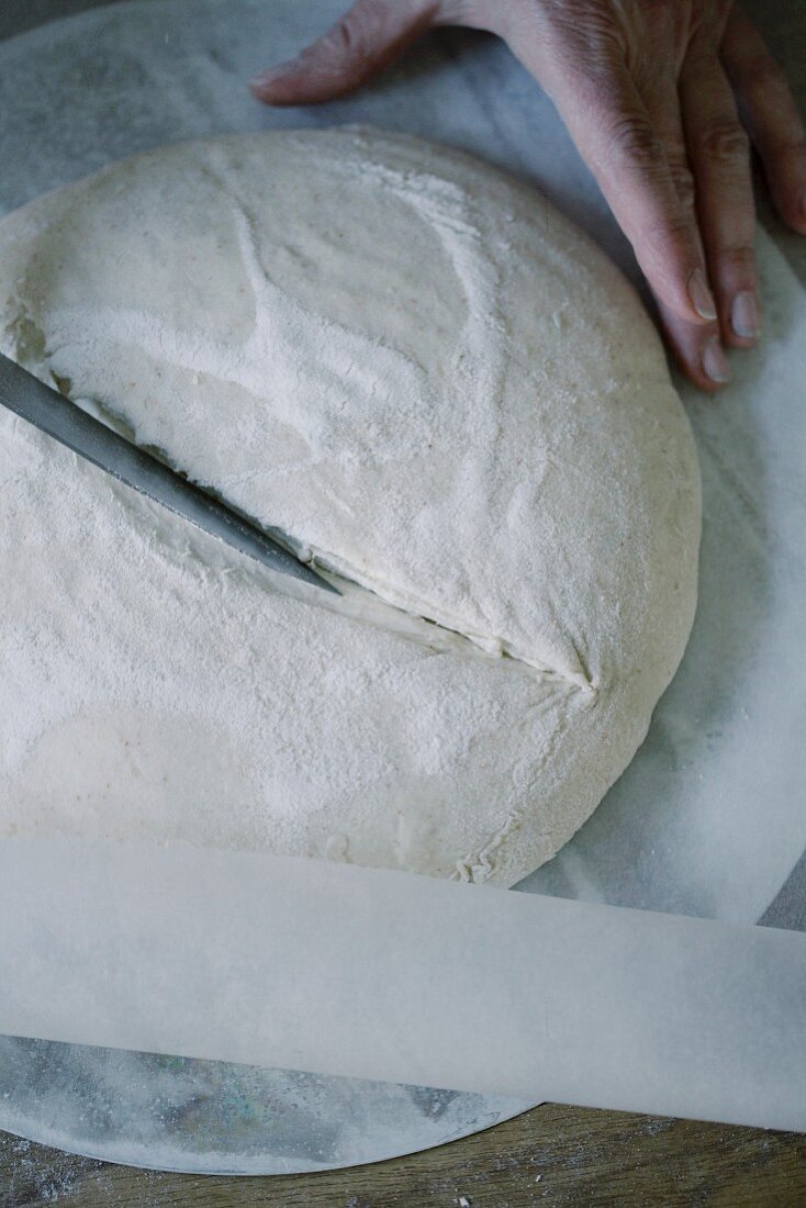 Brotlaib wird vor dem Backen mit einem Messer eingeritzt