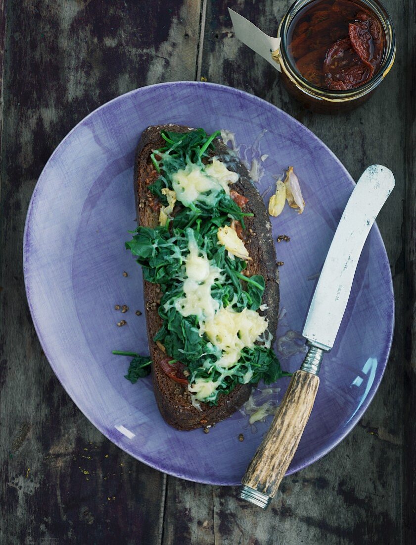 A slice of toasted bread topped with spinach and cheese on a purple plate