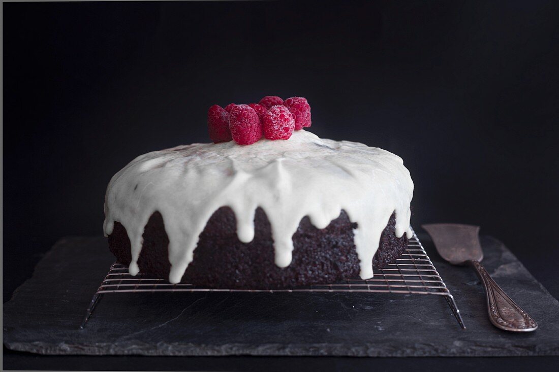 A Red Velvet cake with icing sugar and raspberries on a wire rack