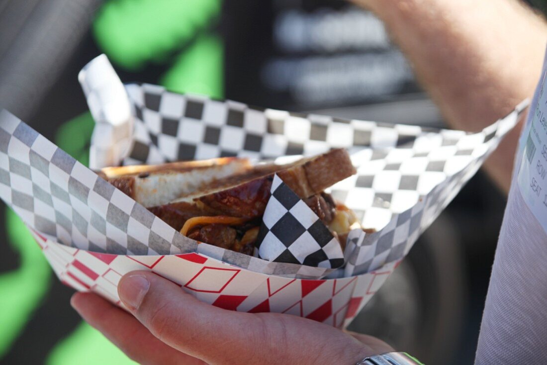 A man holding a cheese sandwich in a paper bag at a food truck festival in California, USA