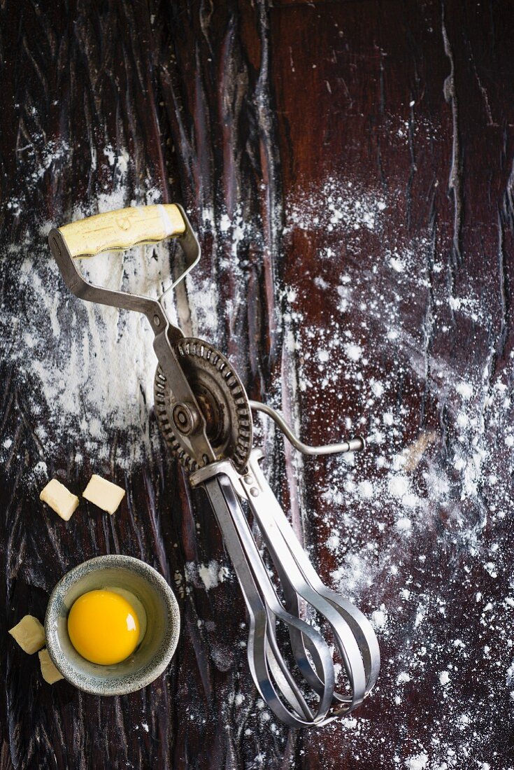 An old hand mixer, flour, a cracked open egg and diced butter