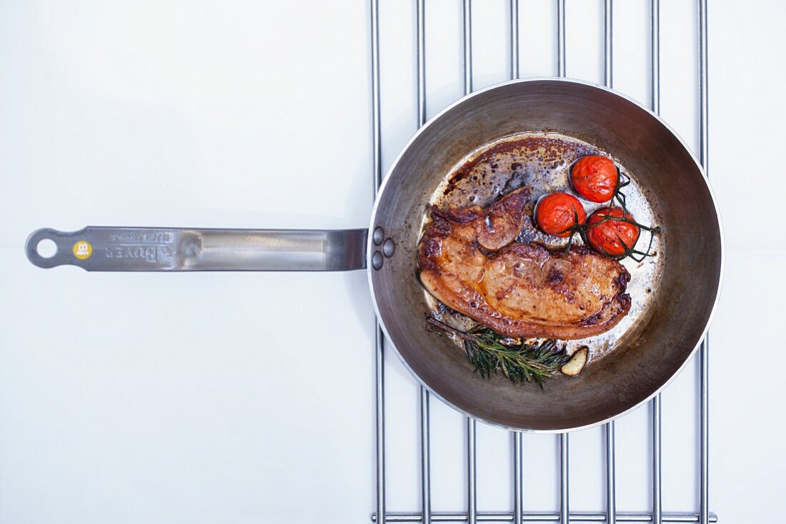 Fried beefsteak with cherry tomatoes and rosemary in a pan (seen from above)
