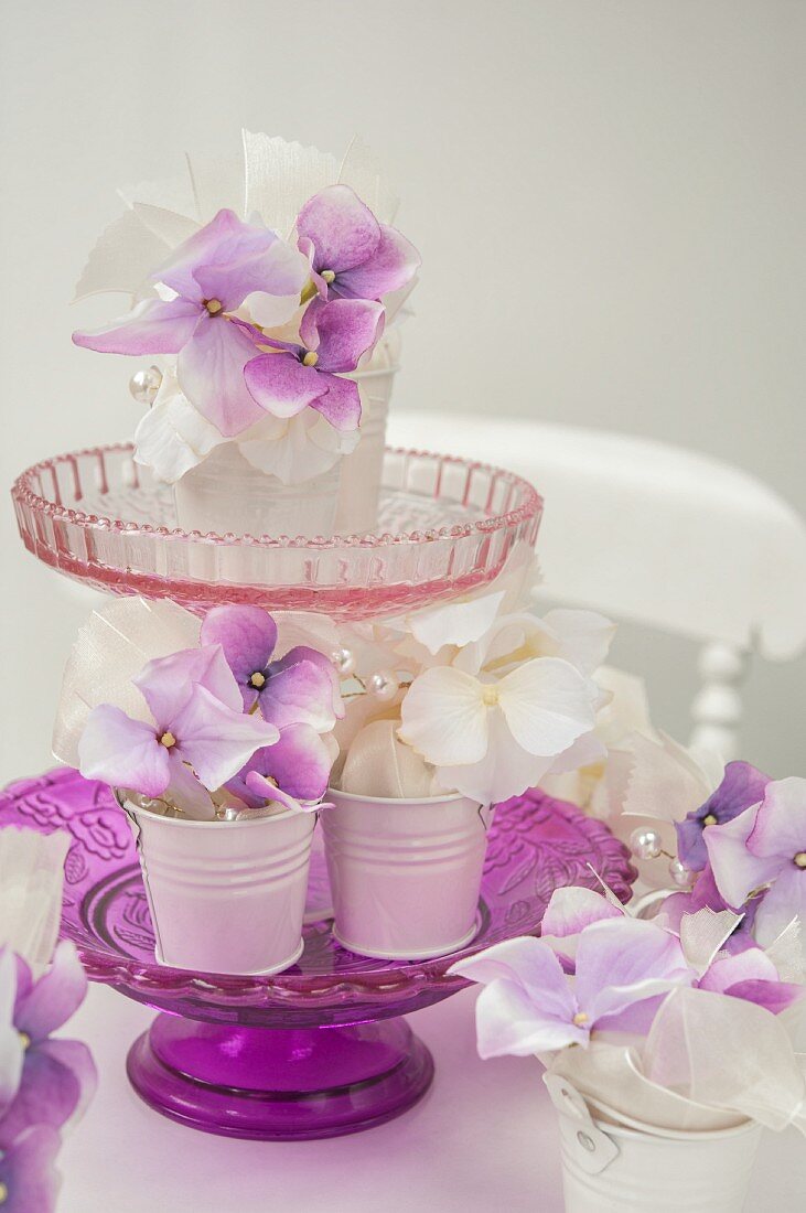 Weiß-violette Hortensienblüten in weissen Metallbehältern auf Etagere aus Glas