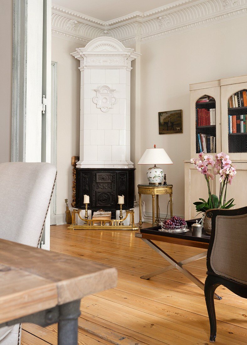 Antique, white tiled stove and elegant round side table in corner of traditional living room