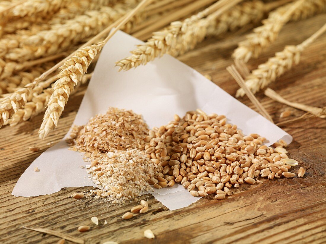 Ears of wheat, wheat seeds, groats and bran on a wooden surface