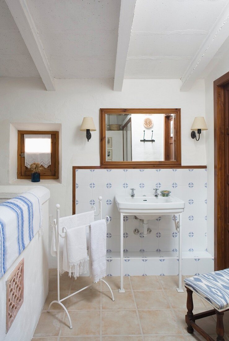 Filigraner Waschtisch vor blau-weiß gefliester Wand, nostalgischer Handtuchhalter mit weissen Handtüchern im Bad