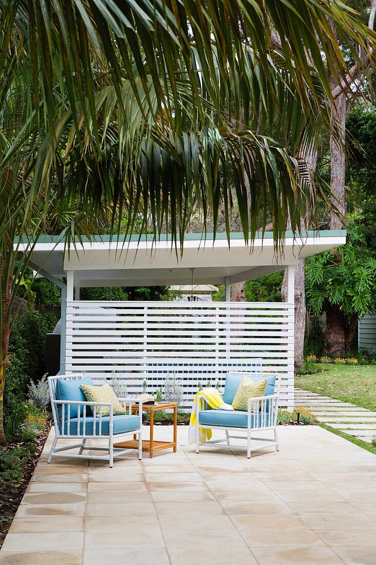 Two armchairs and a side table on a terrace in the palm garden of a beach house